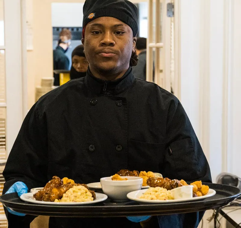 A UPrep culinary student in uniform carrying a service tray