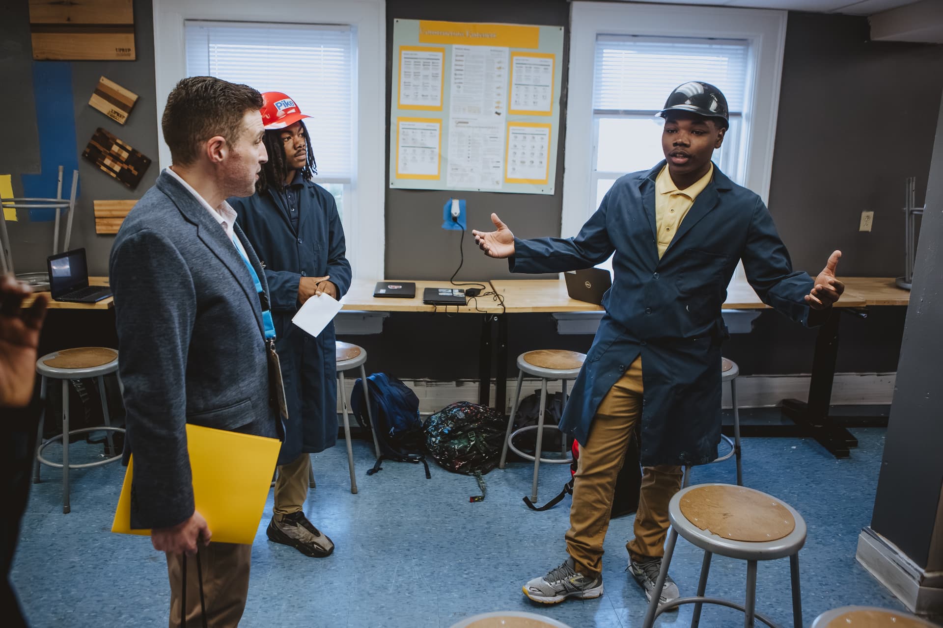 A UPrep student in a lab coat presenting his work to a visitor in a classroom