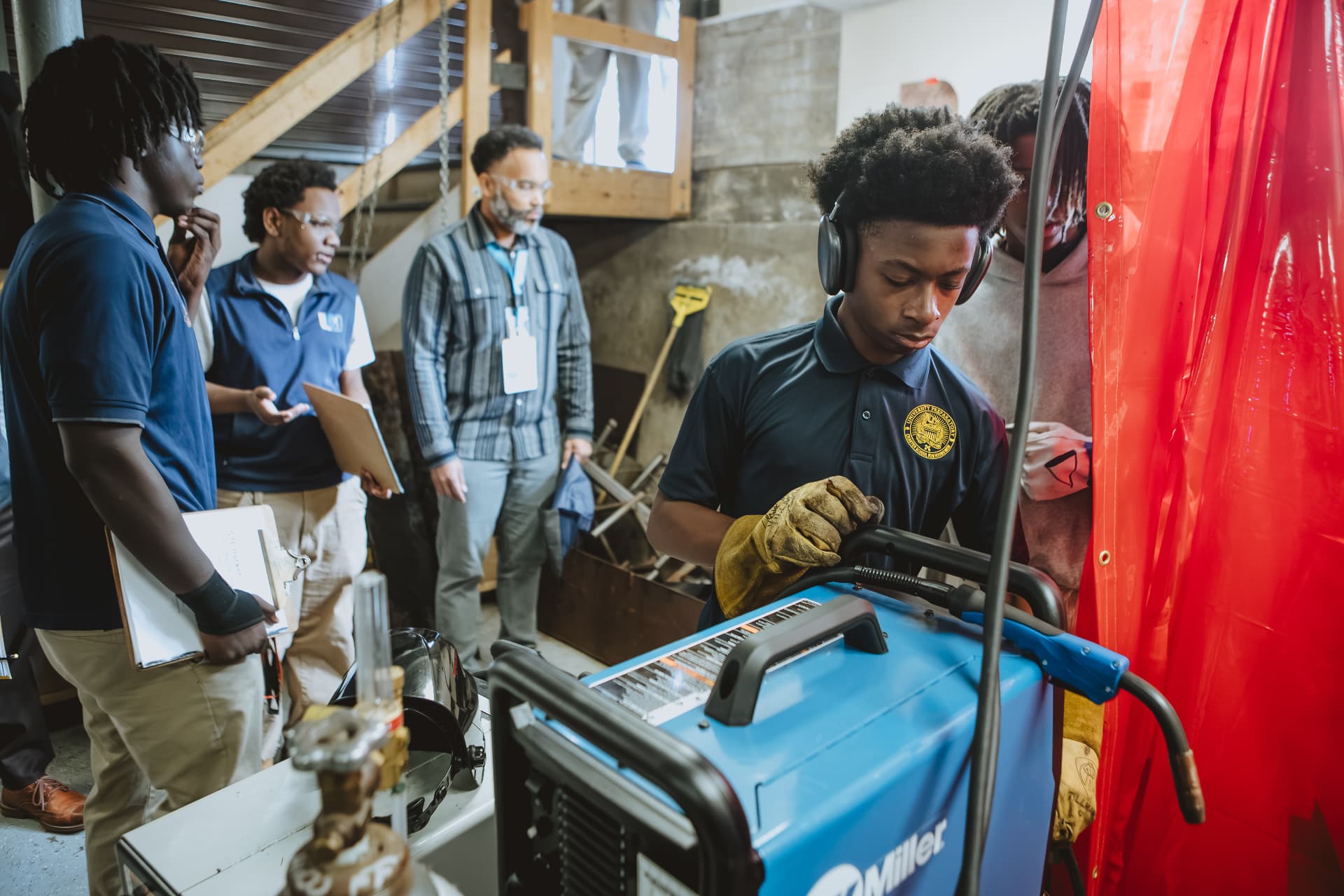 A UPrep student in gloves and headphones operating a welding machine