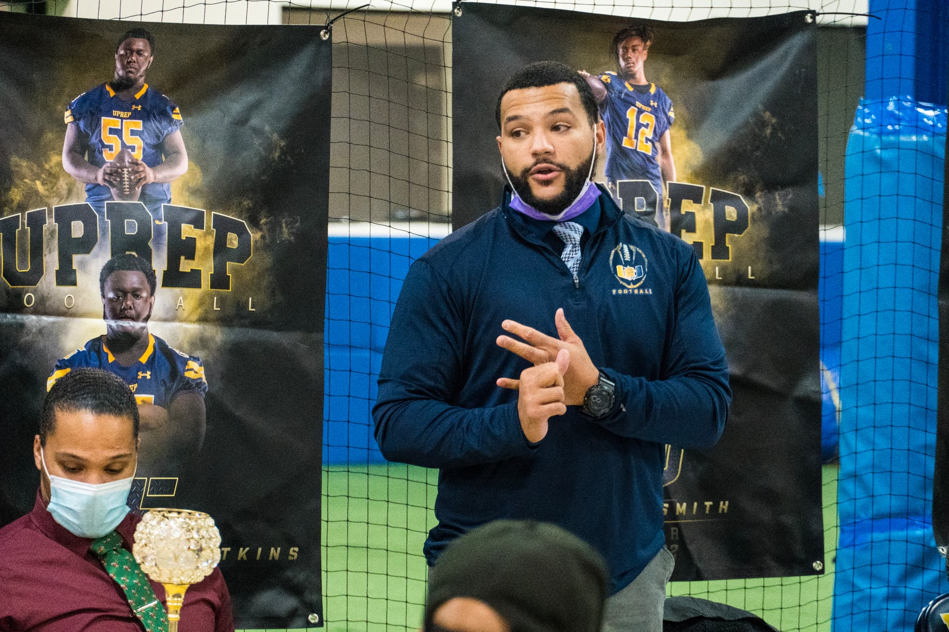 A UPrep football coach speaking in front of team banners