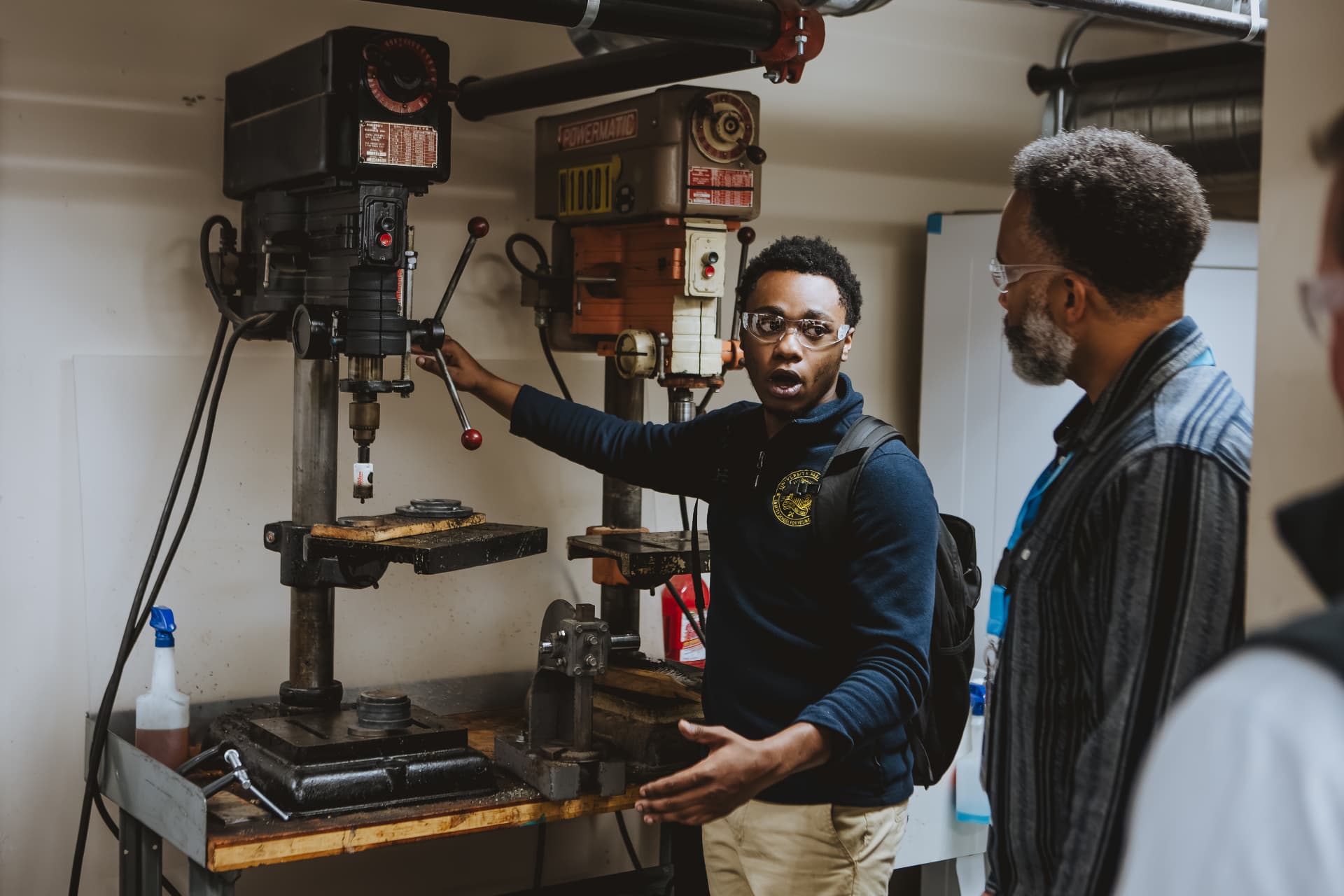 A UPrep student explaining a drill press to a visiting adult in the shop