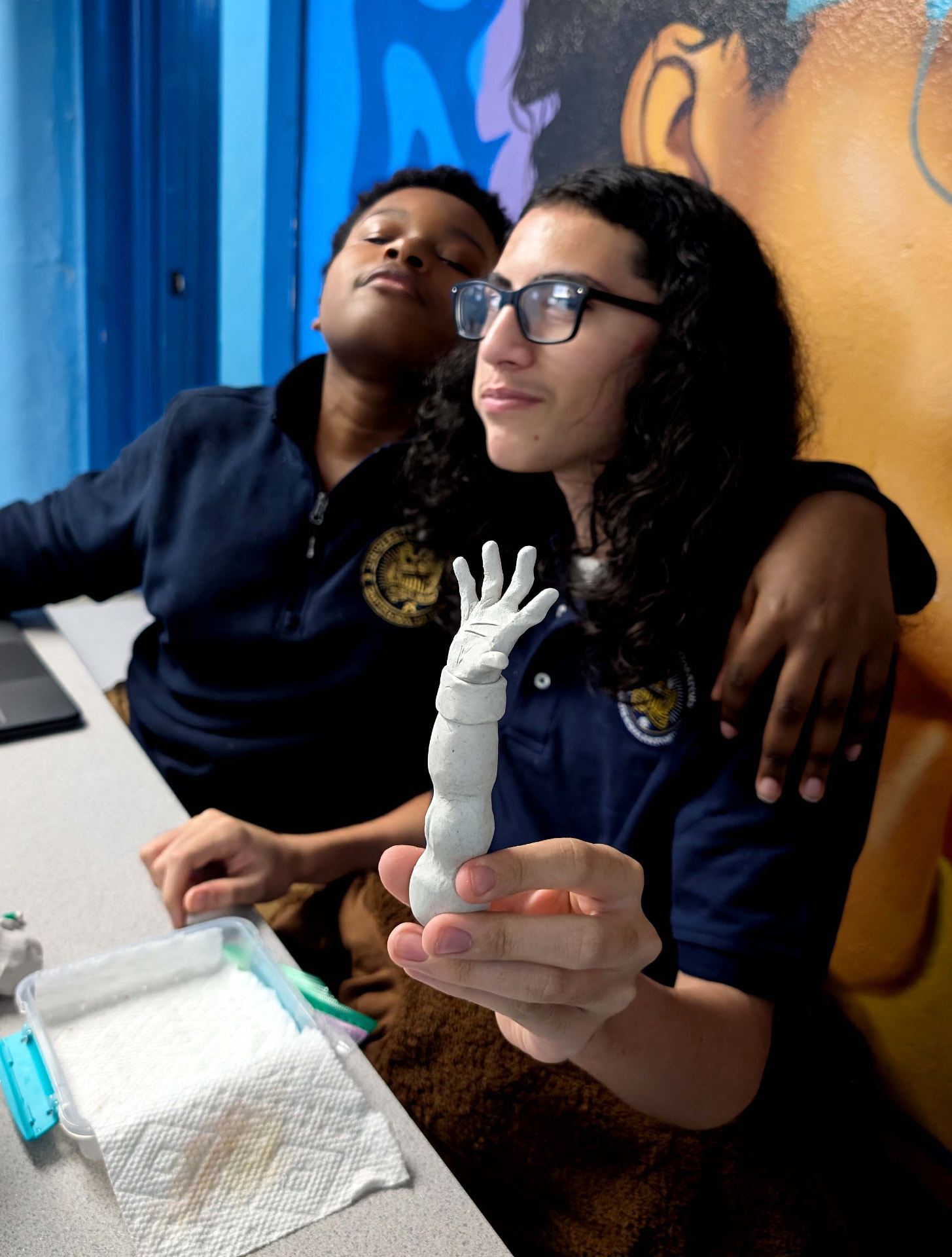 A UPrep student holding up a clay sculpture of a hand beside a classmate